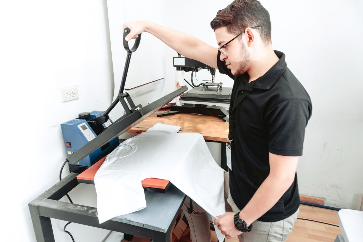 Un homme utilisant une machine pour l'impression par sublimation sur un t-shirt blanc.