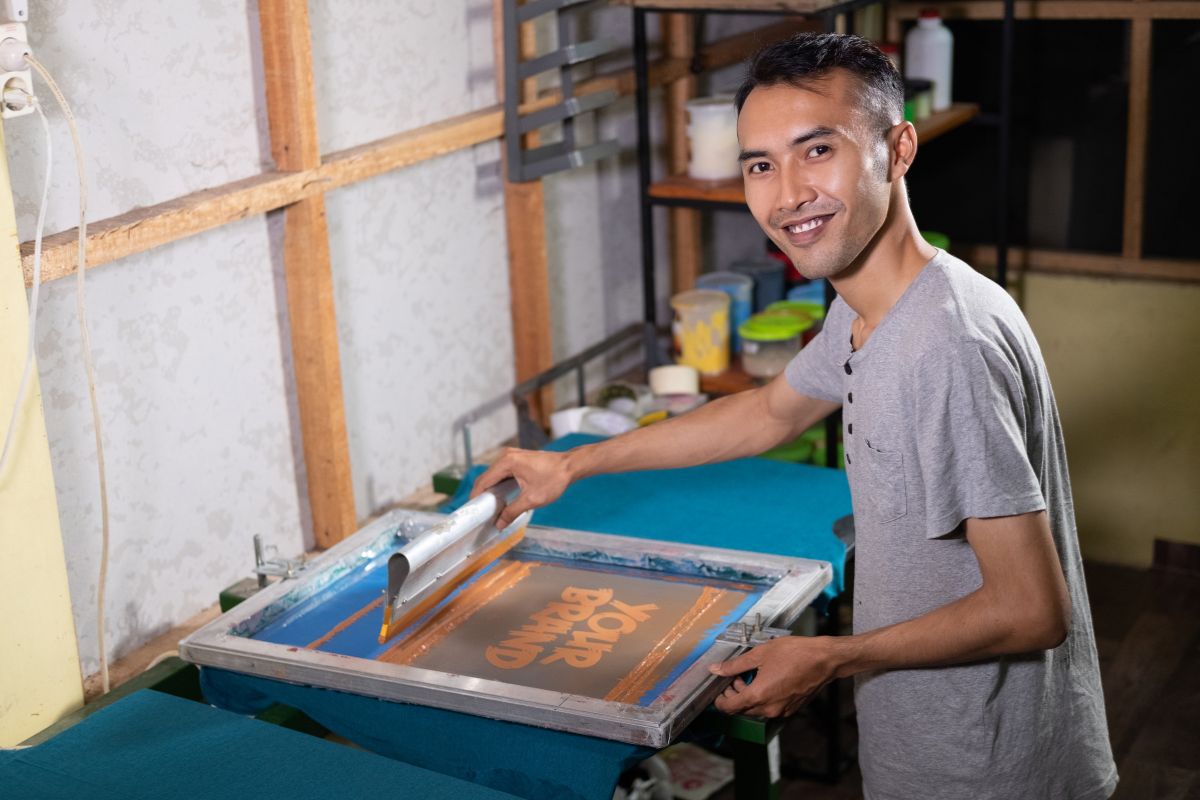 Un homme souriant en train de réaliser une impression sur textile dans un atelier.